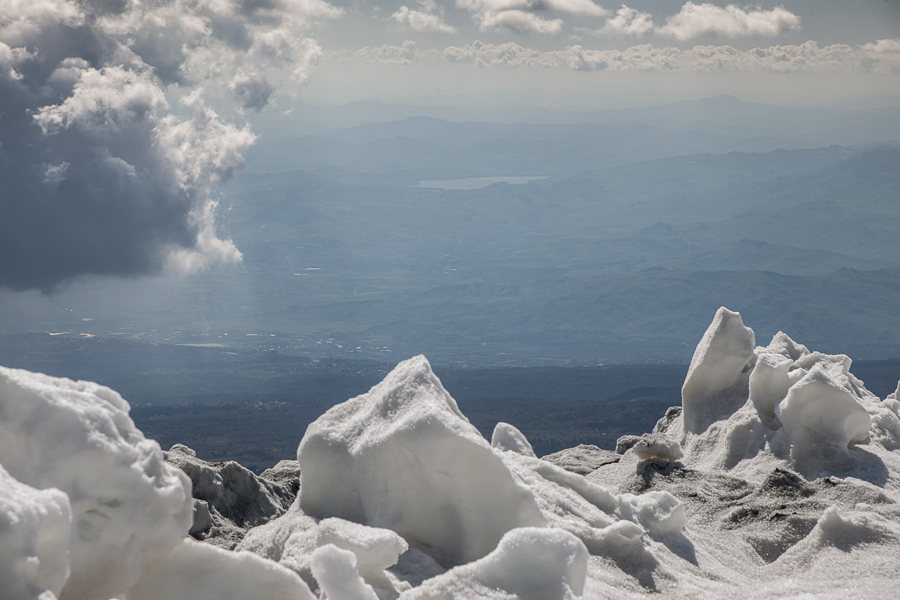 Snow-covered mountain rocks above a broad valley and lake in Sicily